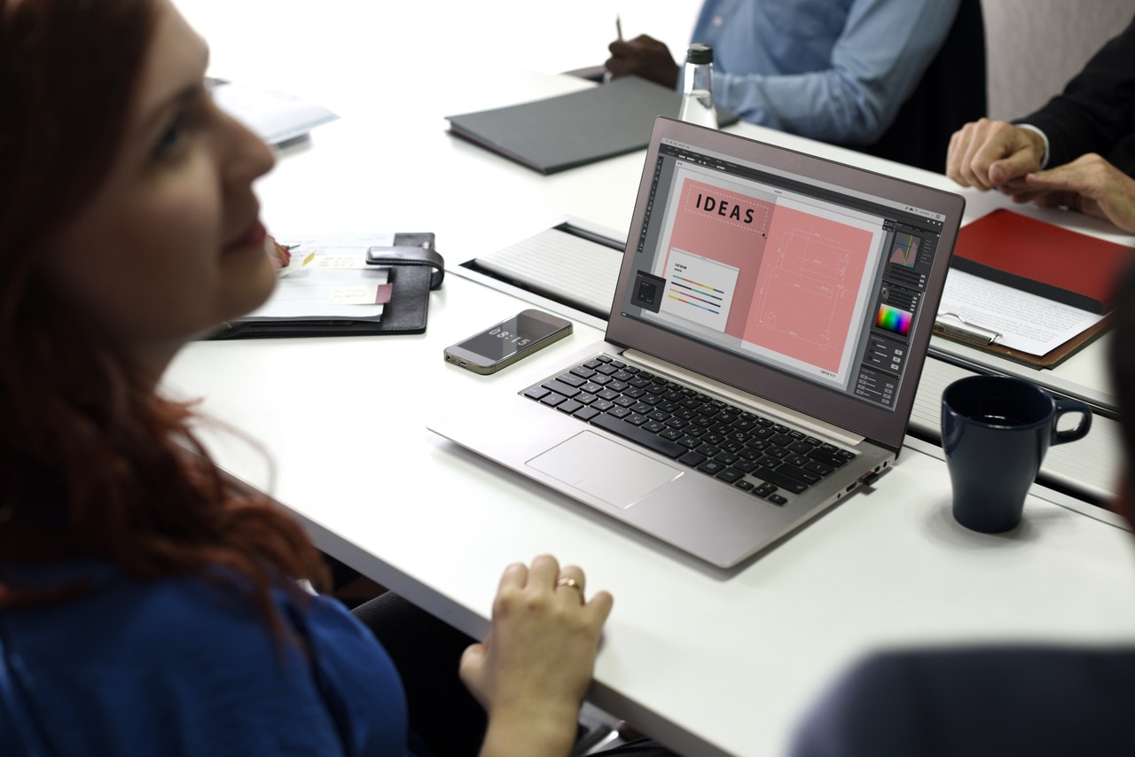 A lady sitting at a laptop. It is placed on a white desk with the word 'IDEAS' written on it