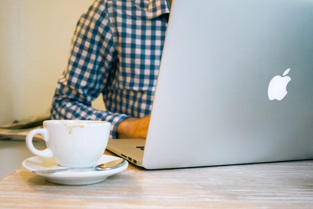 A man sitting on a laptop with a cup beside him 