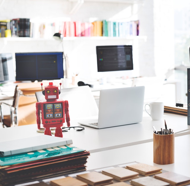 A little robot standing on a desk beside a laptop