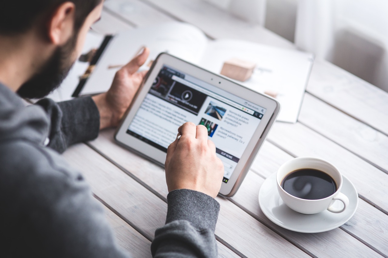 A man sitting with a tablet looking at a web page. 