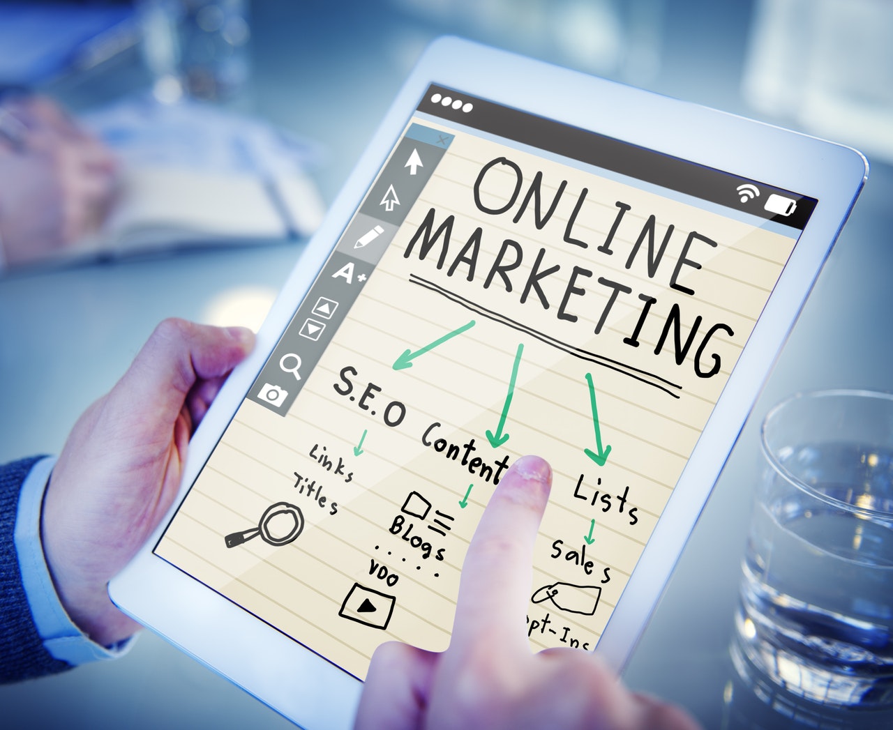 A man holding a white tablet vertically. On the screen it says ONLINE MARKETING in capital letters followed by three arrows leading to the words SEO, Content and Lists.