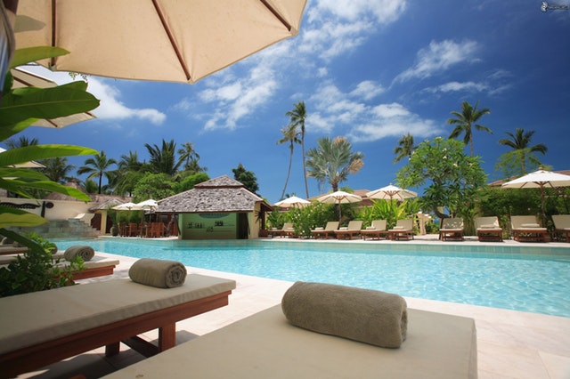 A hotel's swimming pool area with sun loungers around the pool's edge 