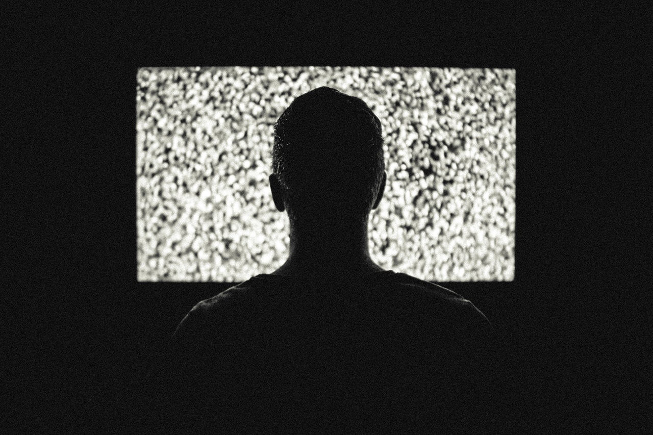 A man staring at a blank and fuzzy TV screen. We can see him from the back looking towards the TV.