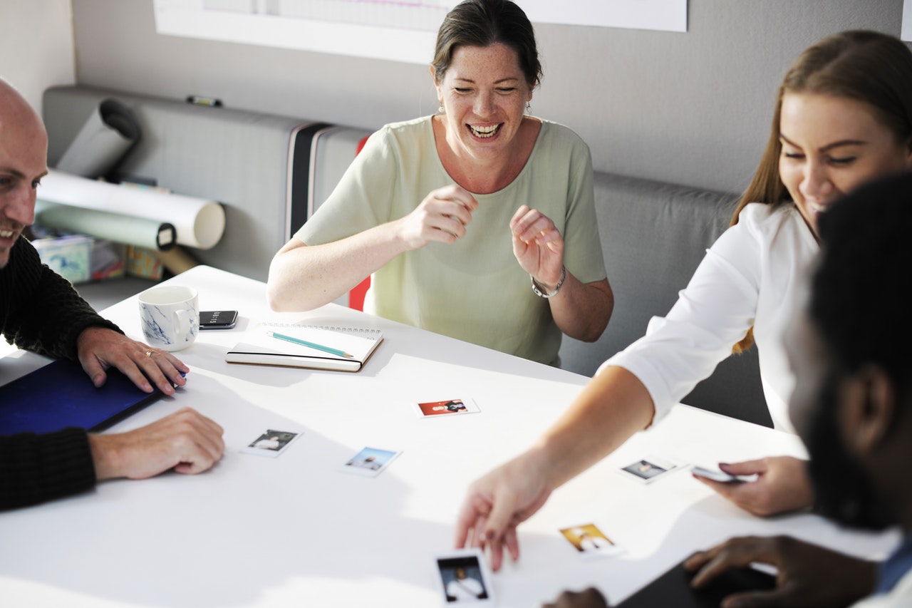 A group of people sat around a white table looking at photographs A group of people sat around a white table looking at photographs