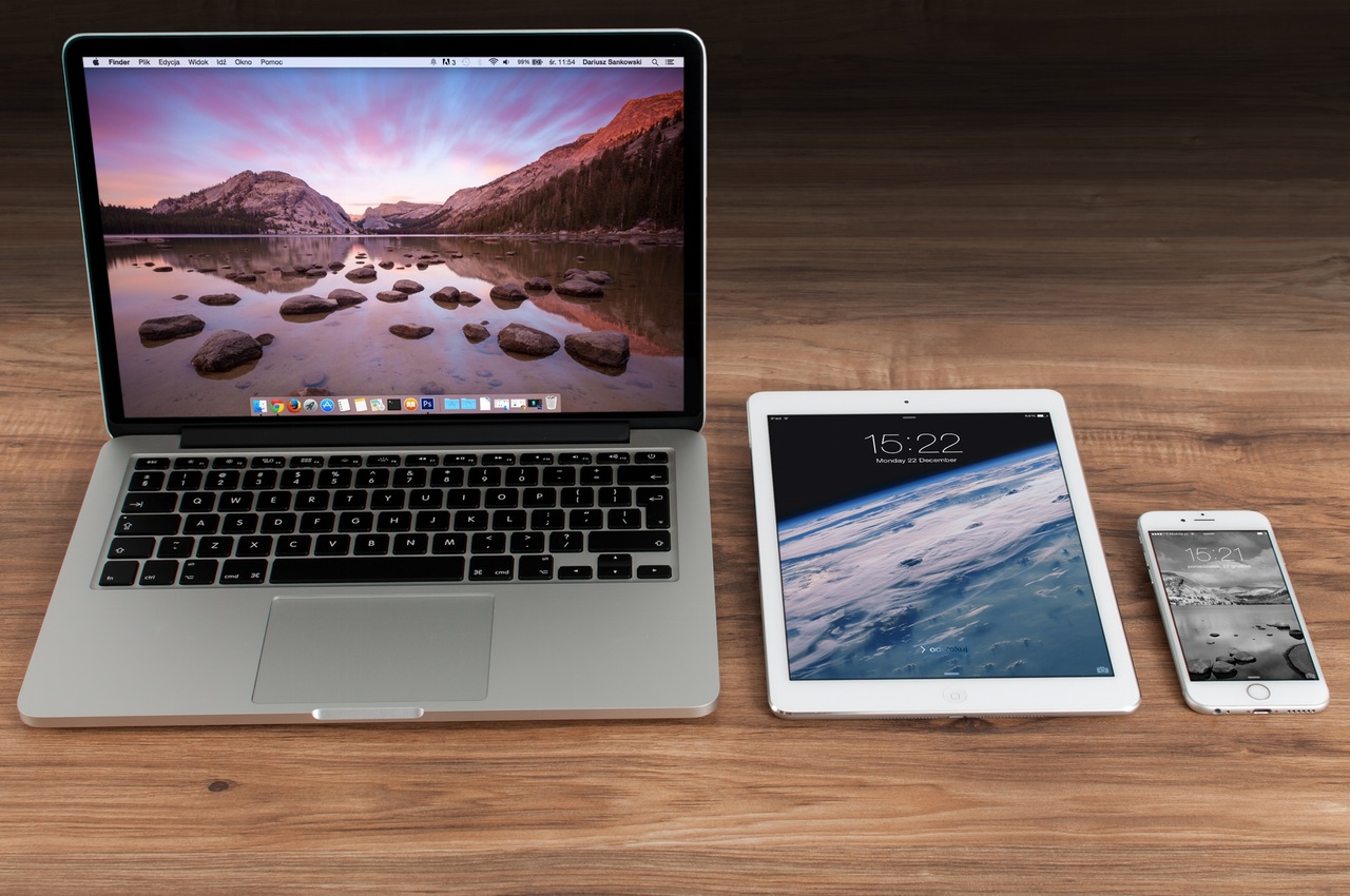 An Apple iPhone, iPad and laptop placed on a desk