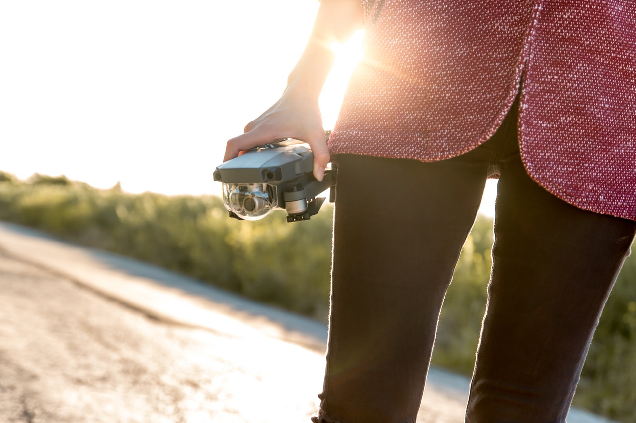 A woman wearing a black pair of trousers and a red and white top holding onto a camera in her right hand 