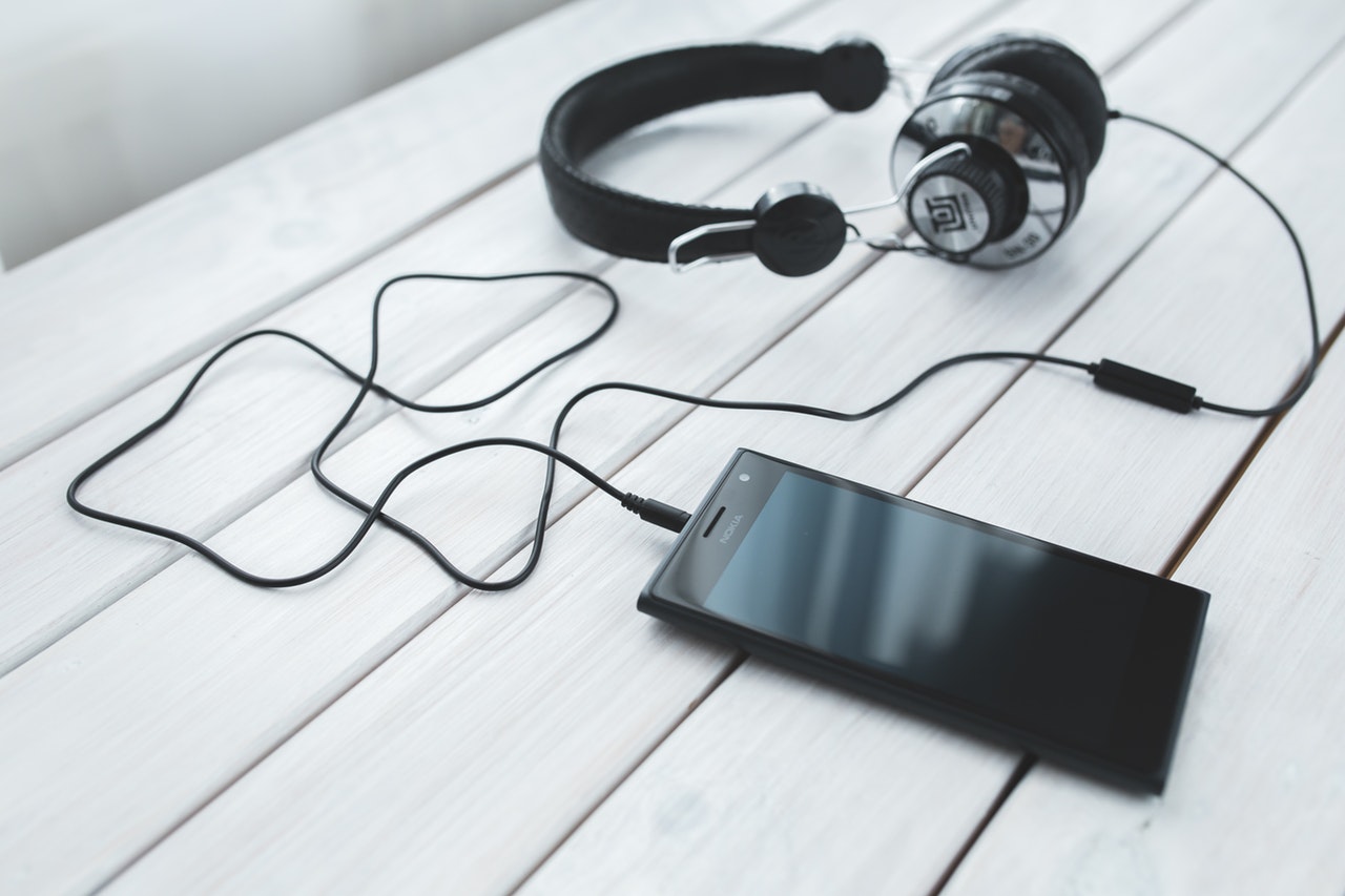 A light wooden bench with a mobile phone placed upon it complete with headphones connected to the phone A light wooden bench with a mobile phone placed upon it complete with headphones connected to the phone