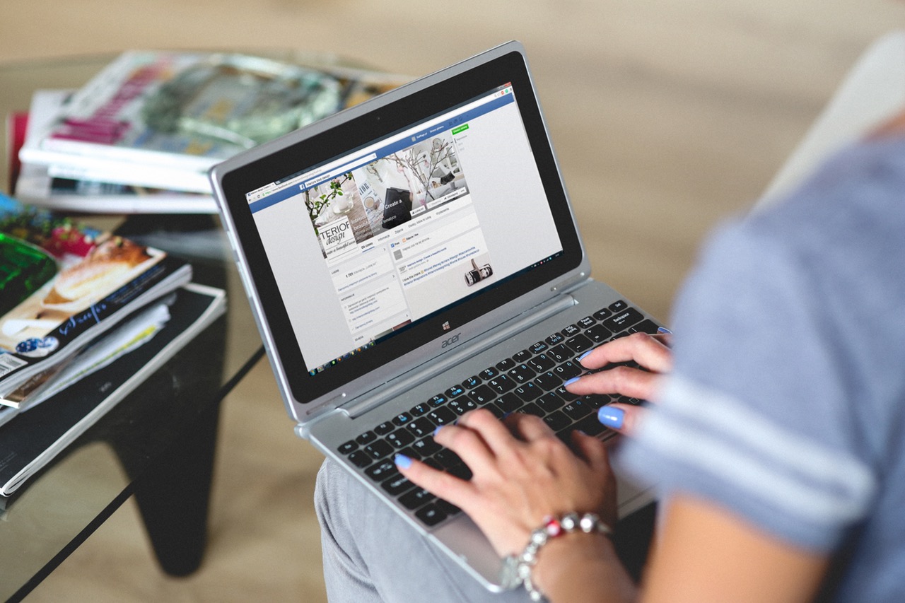 A woman sitting down with a laptop on her lap. She is viewing a Facebook business page A woman sitting down with a laptop on her lap. She is viewing a Facebook business page