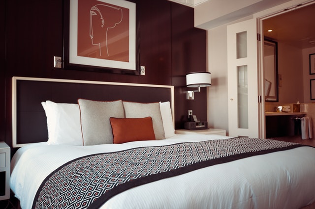 A modern hotel room bed with burgundy background and a shot of the bathroom