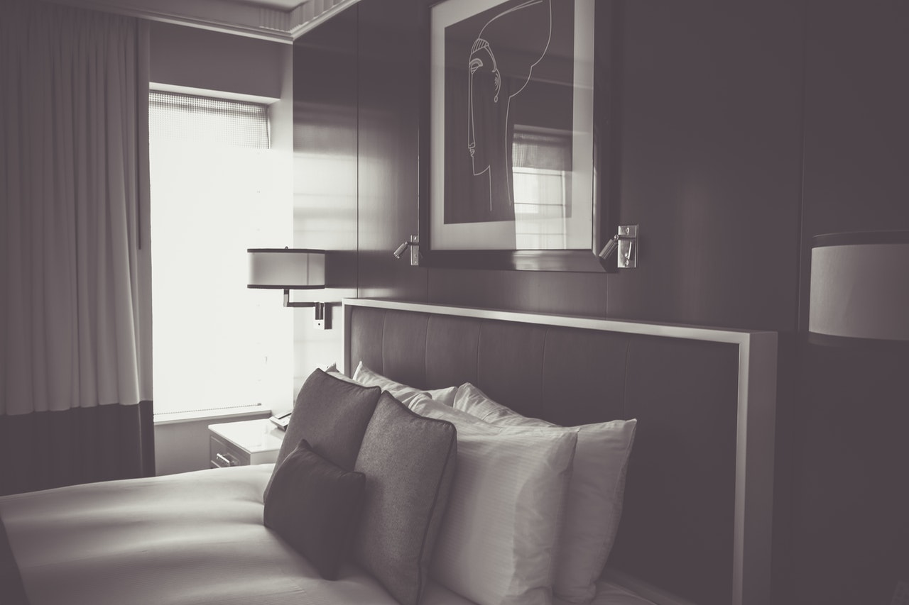 A black and white image of a hotel bed with pillows and cushions, and a framed photo behind it A black and white image of a hotel bed with pillows and cushions, and a framed photo behind it
