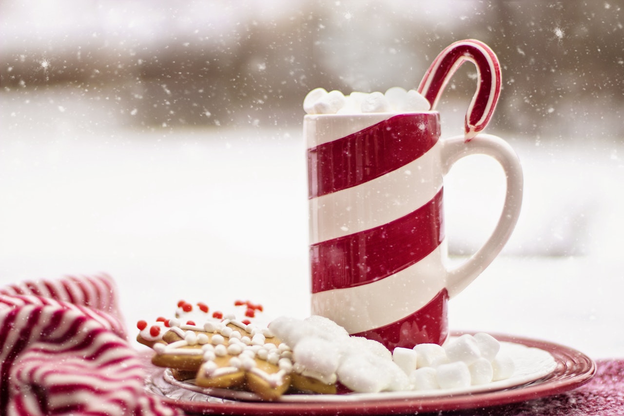 A red and white striped mug on a plate of Christmas-themed cookies and sweets