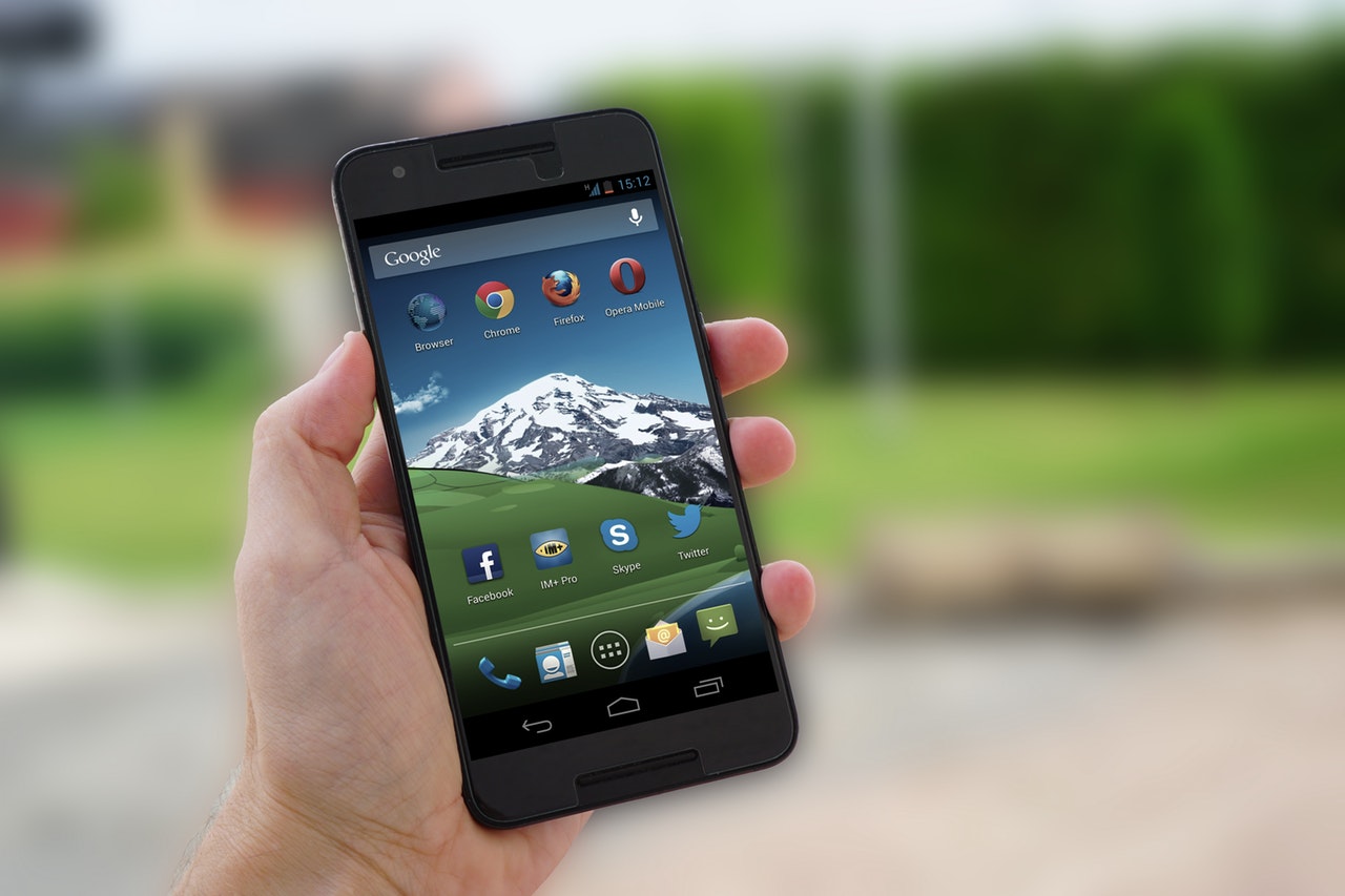 Person holding black Android Smartphone with various apps in the background and a snow-capped mountain as the screensaver 