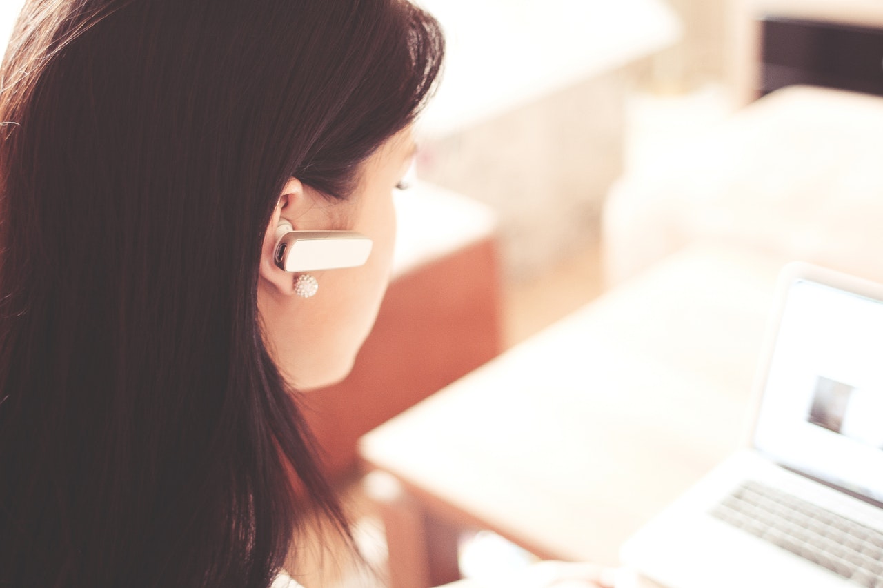 Woman wearing white earpiece using white laptop 