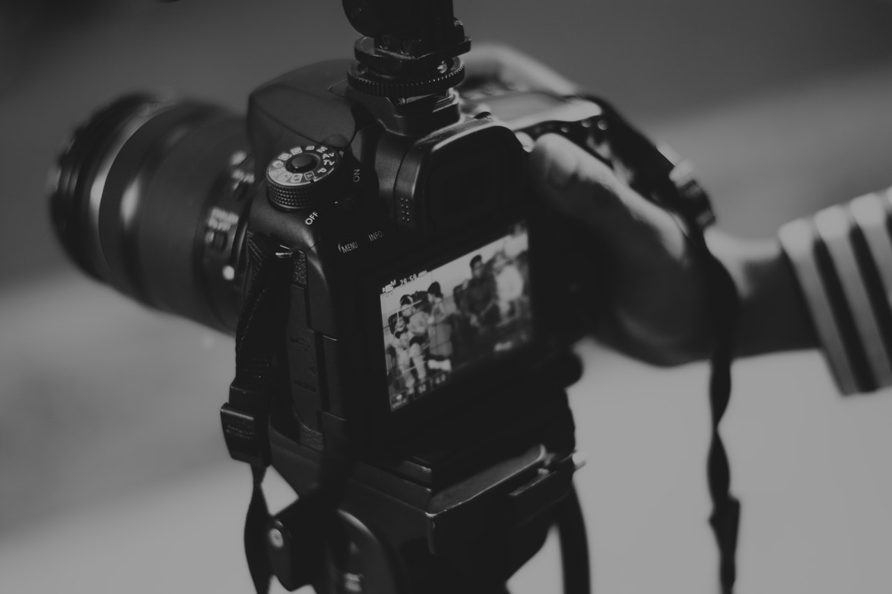 A black and white image of a professional digital camera with a person's hand holding the camera 