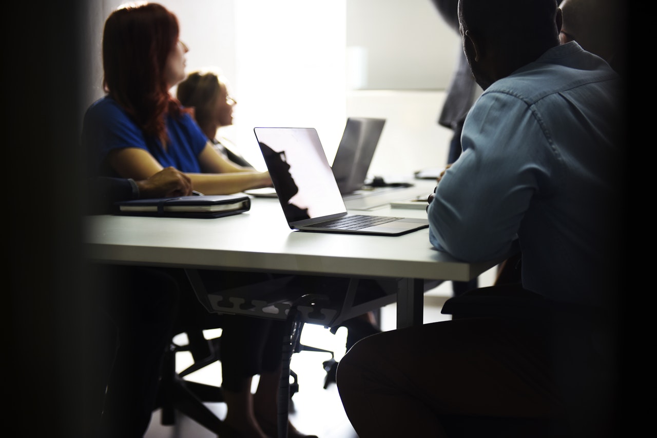 A group of people seated at desks with laptops in front of them A group of people seated at desks with laptops in front of them