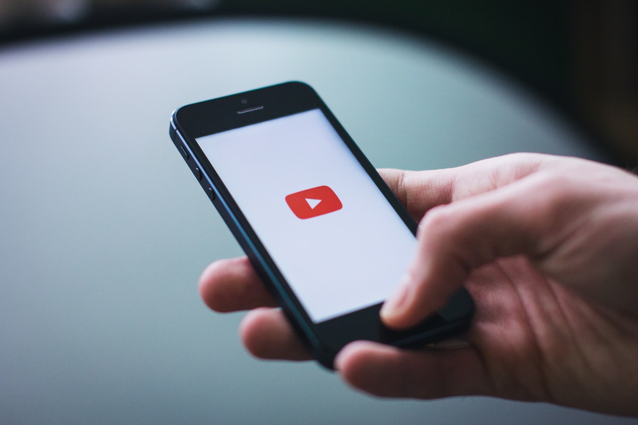 A man holding his mobile phone with the YouTube icon featured on the screen