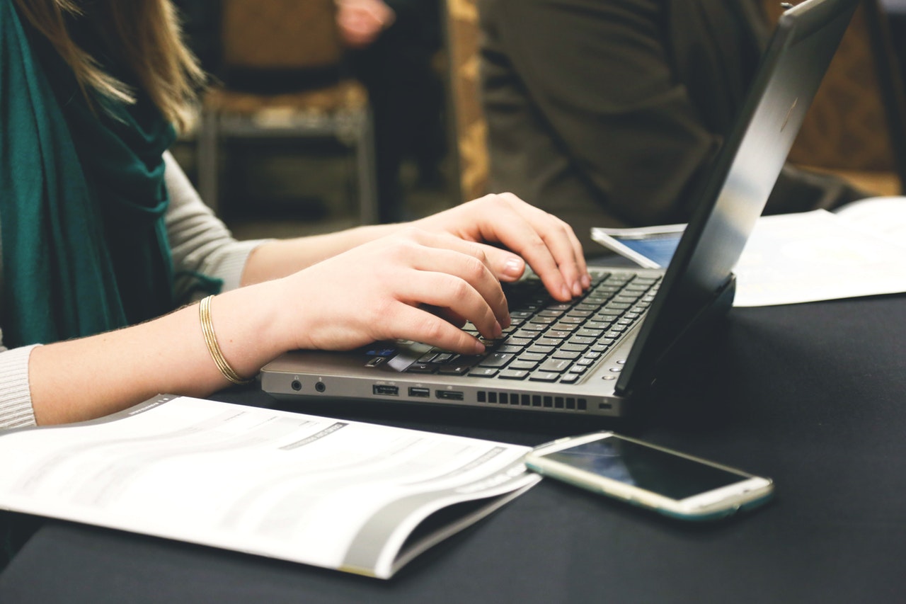 A lady sitting on a laptop. She has a pamphlet beside her and a mobile phone. 