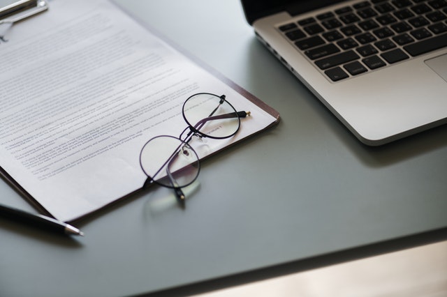 A pair of glasses on a clipboard next to a laptop